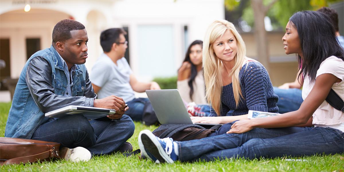Students talk while sitting on college lawn.